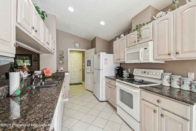 kitchen featuring lofted ceiling, light tile patterned flooring, white appliances, a sink, and dark stone countertops