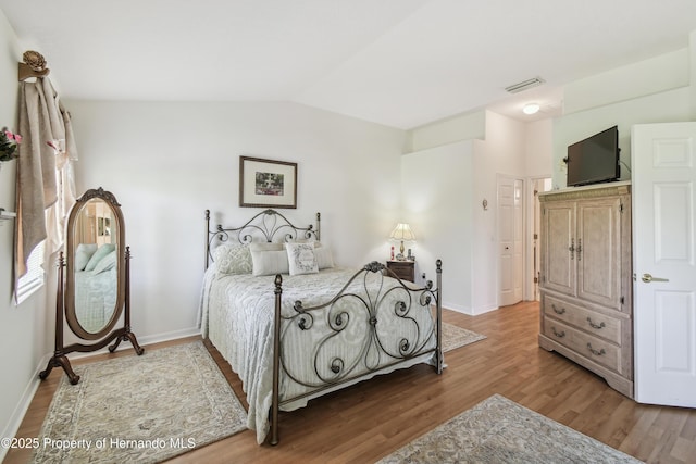 bedroom with baseboards, visible vents, vaulted ceiling, and wood finished floors