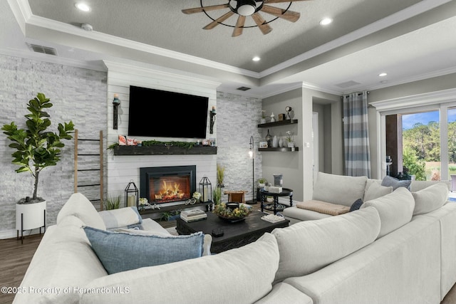 living room featuring a tray ceiling, a fireplace, visible vents, ornamental molding, and wood finished floors