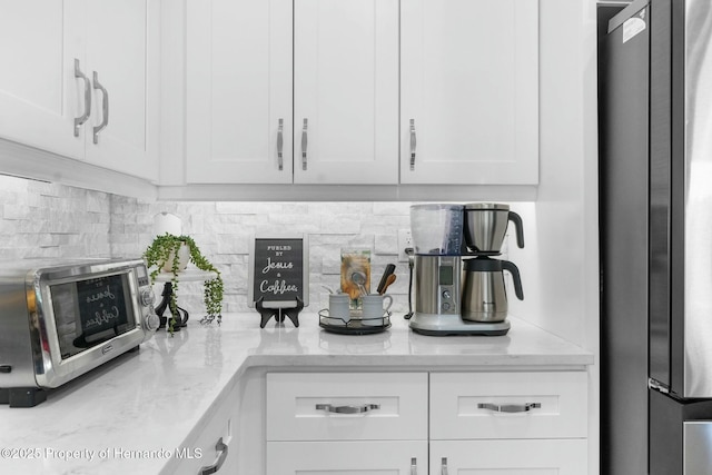 kitchen featuring light stone counters, white cabinetry, stainless steel appliances, and backsplash