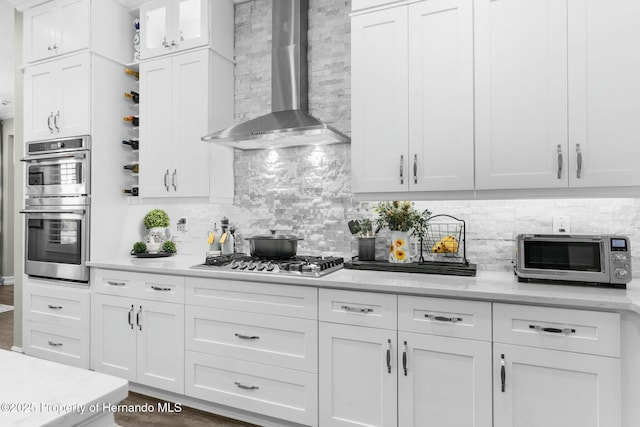 kitchen featuring stainless steel appliances, white cabinets, decorative backsplash, and wall chimney exhaust hood