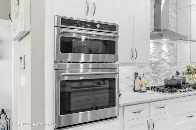 kitchen with white cabinets, wall chimney exhaust hood, stainless steel appliances, and decorative backsplash