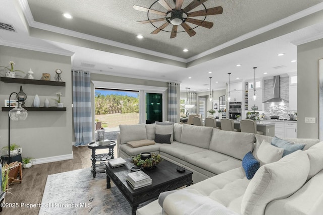 living room with a tray ceiling, wood finished floors, visible vents, and crown molding