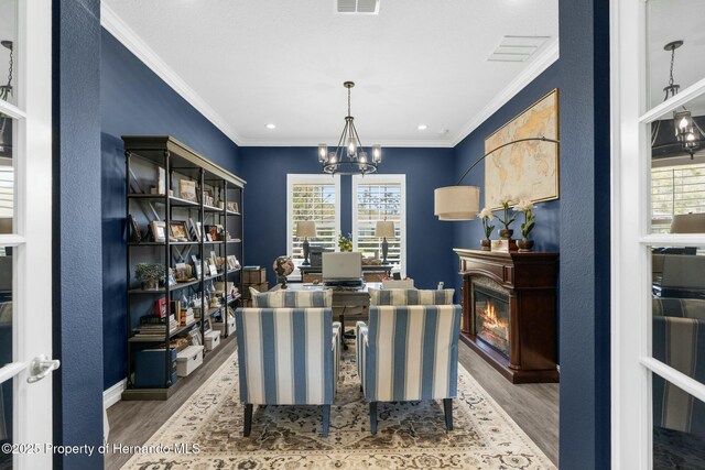 dining space with visible vents, ornamental molding, a glass covered fireplace, wood finished floors, and a chandelier