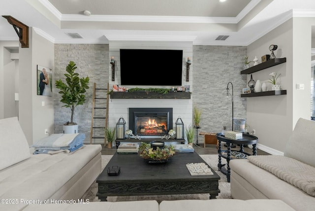 living room with ornamental molding, a tray ceiling, a large fireplace, and visible vents