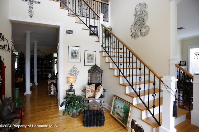 stairway with visible vents, crown molding, ornate columns, and wood finished floors