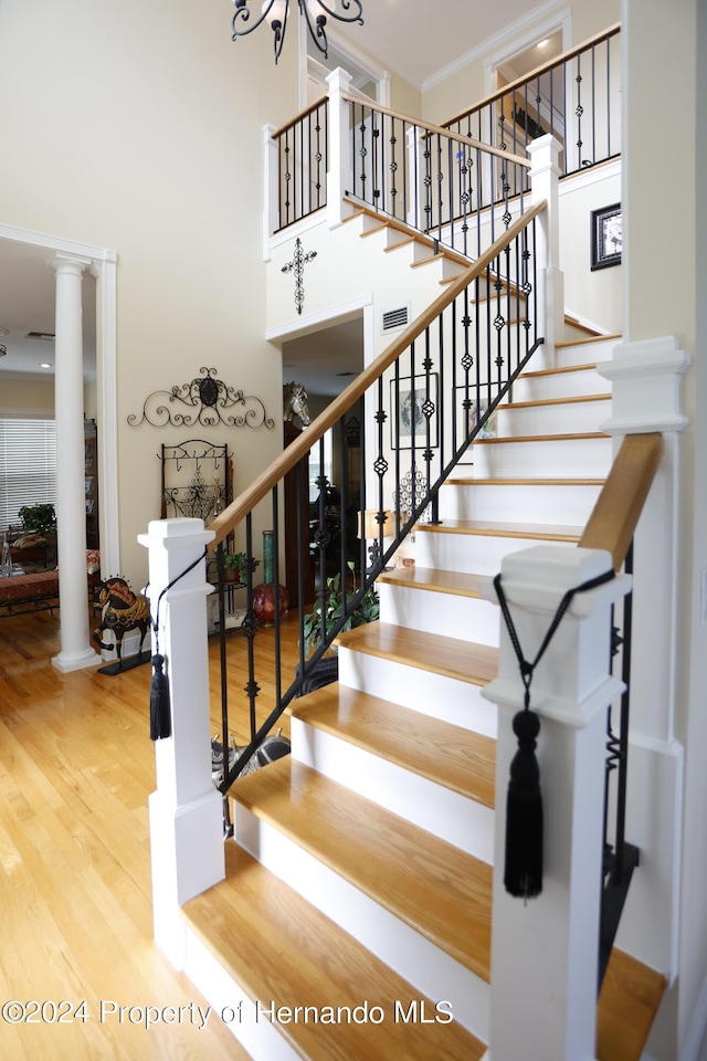 staircase with crown molding, a high ceiling, wood finished floors, and ornate columns