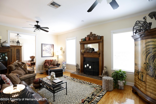 living room featuring a fireplace with raised hearth, crown molding, visible vents, and wood finished floors