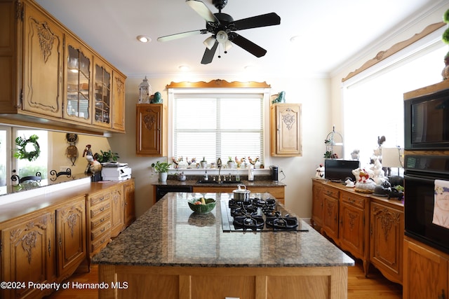 kitchen featuring a sink, ornamental molding, a center island, black appliances, and glass insert cabinets