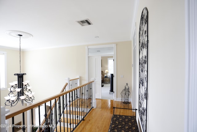 hall with light wood-style flooring, visible vents, crown molding, and an upstairs landing