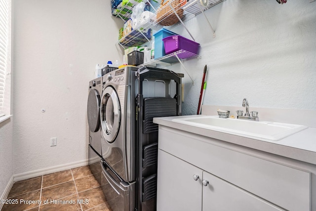 washroom with a textured wall, tile patterned flooring, washing machine and dryer, a sink, and baseboards