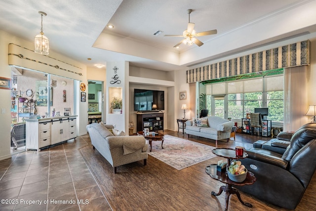 living room featuring baseboards, a raised ceiling, a ceiling fan, and crown molding