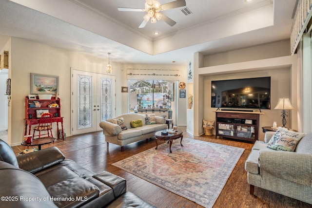 living area featuring french doors, a raised ceiling, visible vents, ornamental molding, and wood finished floors