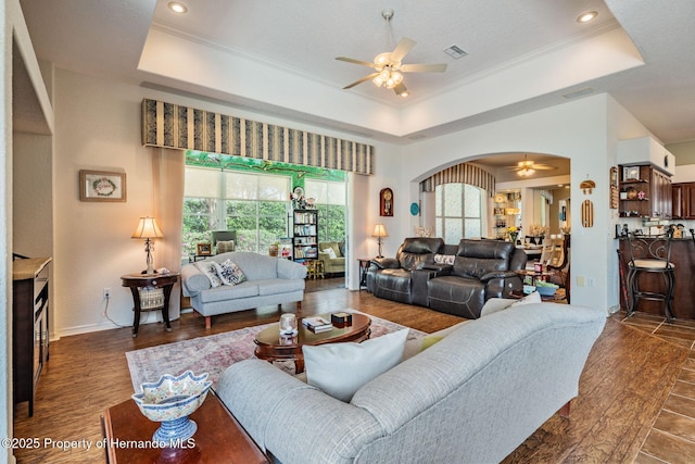 living area with ceiling fan, arched walkways, and a raised ceiling