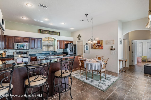 kitchen with visible vents, arched walkways, dark countertops, appliances with stainless steel finishes, and a breakfast bar area