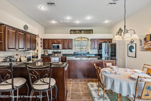 kitchen with visible vents, dark countertops, a peninsula, stainless steel appliances, and backsplash