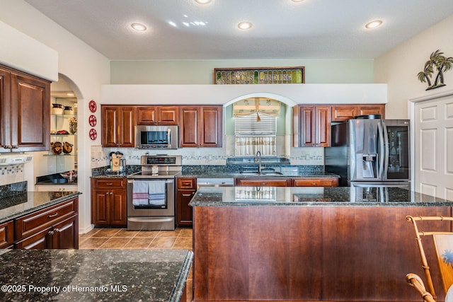 kitchen featuring light tile patterned floors, arched walkways, decorative backsplash, stainless steel appliances, and a sink