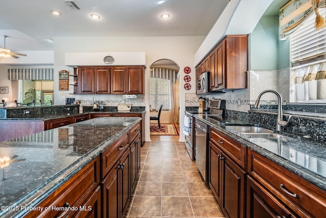 kitchen featuring arched walkways, stainless steel appliances, visible vents, decorative backsplash, and a sink