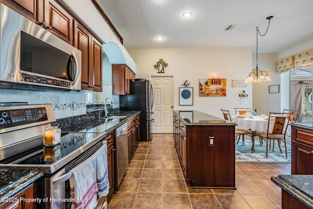 kitchen with decorative backsplash, dark stone countertops, a center island, stainless steel appliances, and a sink