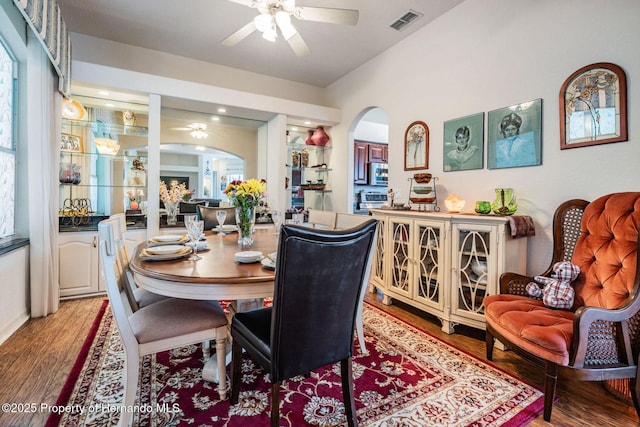 dining space featuring arched walkways, wood finished floors, visible vents, and a ceiling fan