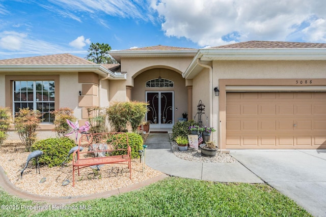 view of front of house featuring french doors, roof with shingles, stucco siding, a garage, and driveway