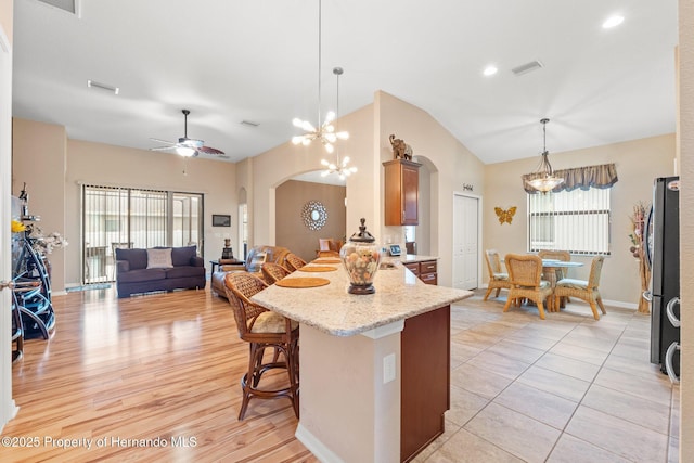 kitchen featuring visible vents, arched walkways, lofted ceiling, a peninsula, and a kitchen bar