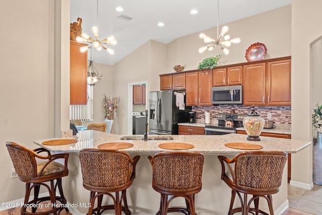 kitchen featuring light stone counters, stainless steel appliances, an inviting chandelier, brown cabinetry, and a sink