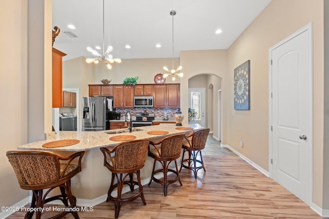 kitchen featuring arched walkways, brown cabinetry, independent washer and dryer, stainless steel appliances, and a sink