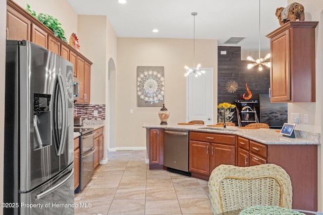 kitchen featuring brown cabinets, backsplash, appliances with stainless steel finishes, a sink, and a chandelier