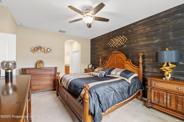 carpeted bedroom with a ceiling fan, arched walkways, visible vents, and wooden walls