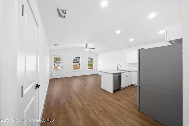 kitchen with lofted ceiling, a peninsula, a sink, open floor plan, and appliances with stainless steel finishes