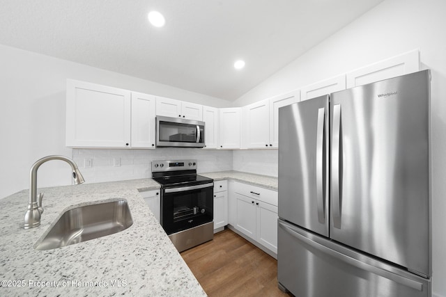 kitchen with stainless steel appliances, lofted ceiling, decorative backsplash, white cabinetry, and a sink