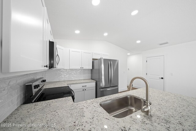 kitchen featuring stainless steel appliances, vaulted ceiling, a sink, and light stone counters