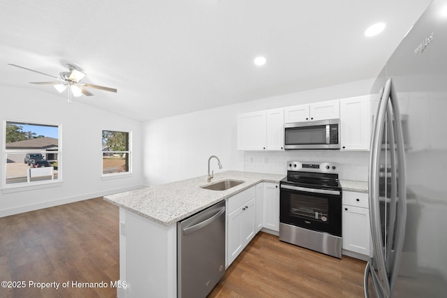 kitchen with stainless steel appliances, vaulted ceiling, a sink, wood finished floors, and a peninsula