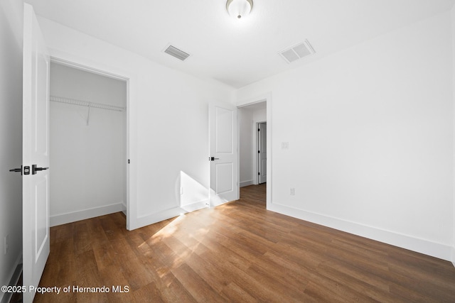 unfurnished bedroom featuring a closet, wood finished floors, visible vents, and baseboards