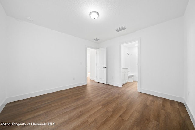 unfurnished bedroom with ensuite bathroom, wood finished floors, visible vents, and baseboards