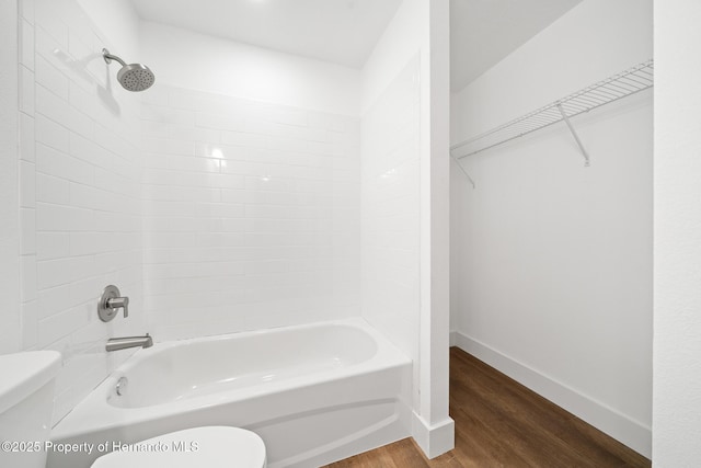 full bath with a spacious closet, toilet, wood finished floors,  shower combination, and baseboards