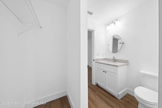 half bath featuring visible vents, toilet, vanity, wood finished floors, and baseboards