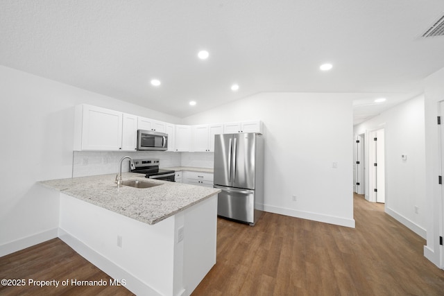 kitchen with stainless steel appliances, a peninsula, a sink, vaulted ceiling, and dark wood finished floors