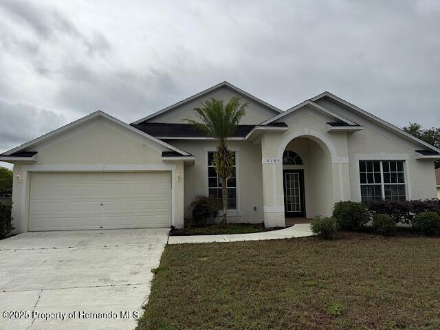 5165 Greystone Dr, Spring Hill, FL 34609 - ranch-style house with an attached garage, concrete driveway, stucco siding, and a front lawn