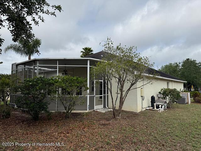 5165 Greystone Dr, Spring Hill, FL 34609 - back of property with a sunroom, stucco siding, and a lawn