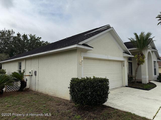 5165 Greystone Dr, Spring Hill, FL 34609 - view of side of home featuring concrete driveway, an attached garage, and stucco siding