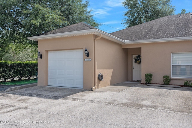 ranch-style home featuring a garage, stucco siding, driveway, and roof with shingles