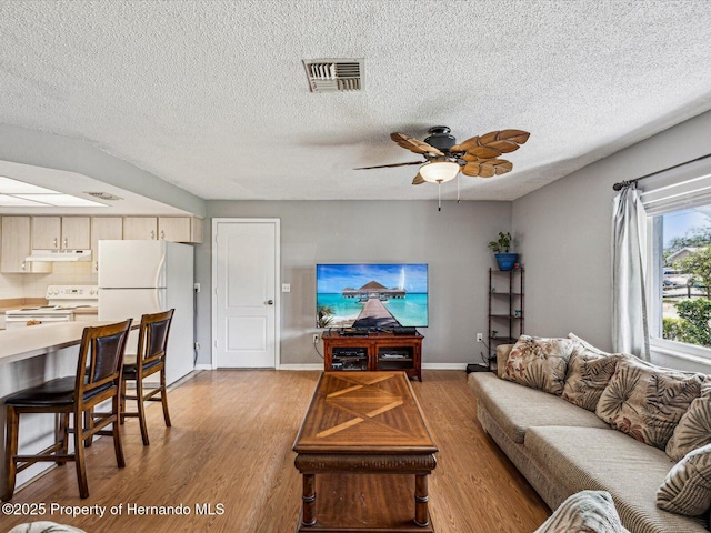 living room featuring ceiling fan, a textured ceiling, visible vents, baseboards, and light wood-type flooring