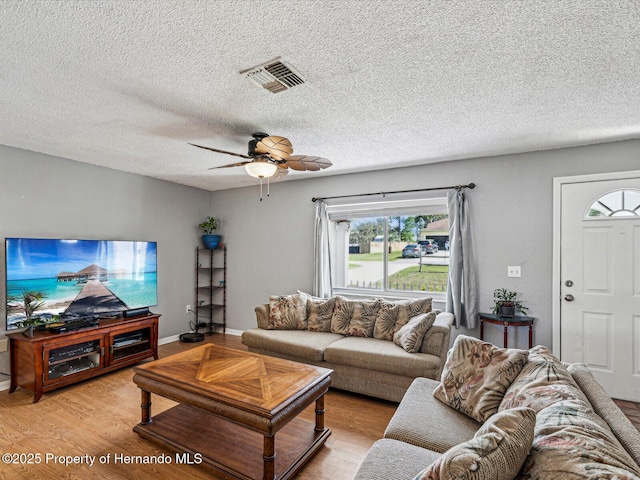 living area with light wood finished floors, visible vents, baseboards, ceiling fan, and a textured ceiling