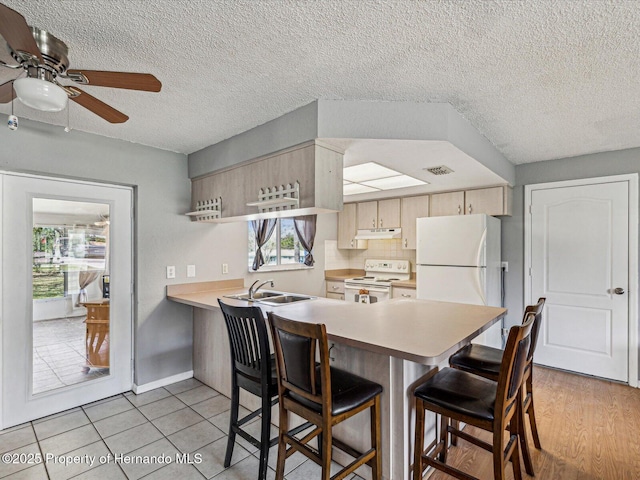 kitchen featuring light countertops, a peninsula, white appliances, under cabinet range hood, and a kitchen breakfast bar