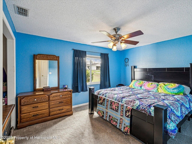 carpeted bedroom with a textured ceiling, visible vents, a ceiling fan, and a textured wall