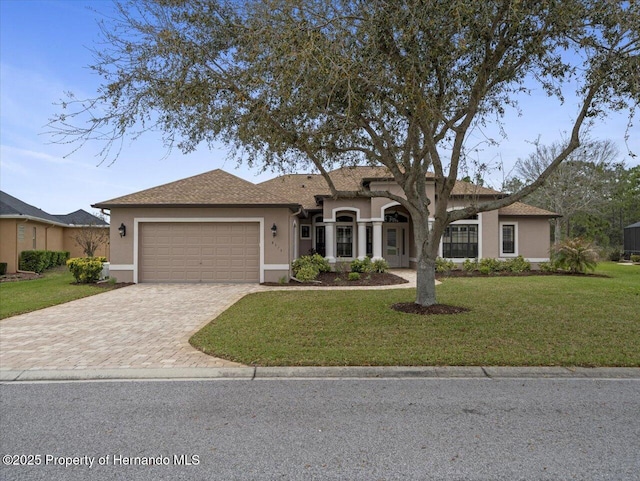 view of front facade featuring a garage, decorative driveway, a front yard, and stucco siding