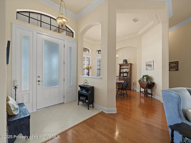 entrance foyer with arched walkways, wood finished floors, visible vents, baseboards, and crown molding