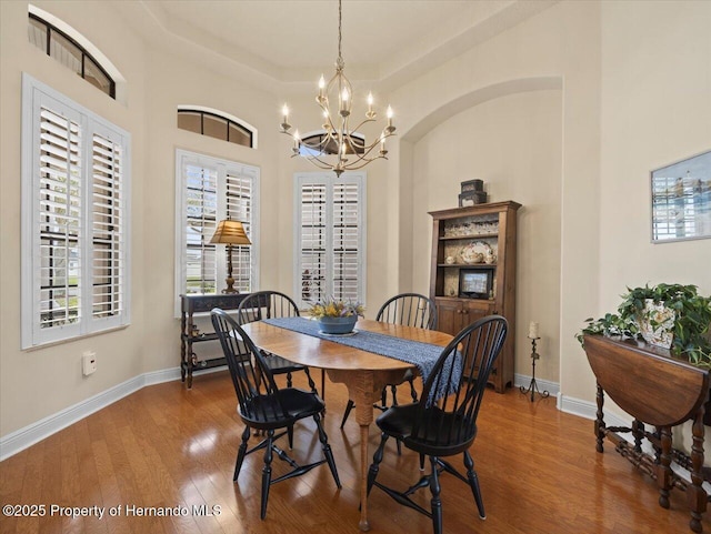 dining space featuring a chandelier, a raised ceiling, baseboards, and wood finished floors